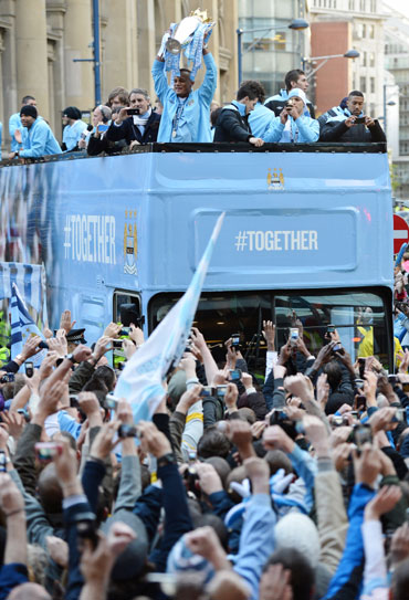 Manchester City captain Vincent Kompany (C) hows off the Barclays Premier League trophy in front of thousands of fans during their victory parade around the streets of Manchester