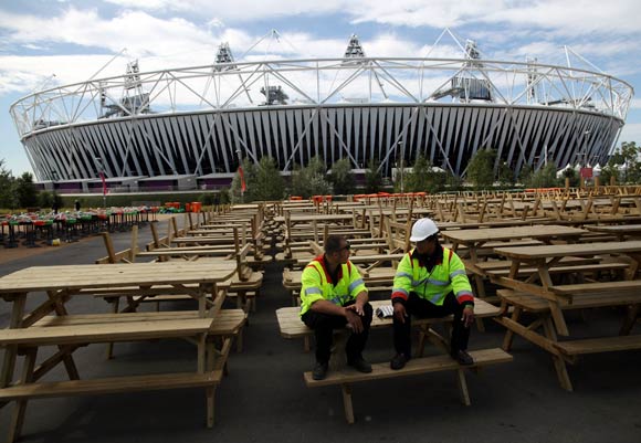 Workmen take a break on a row of upturned benches outside the Olympic Stadium in Stratford, East London