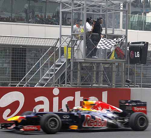 Gagan Narang waves the flag as Red Bull driver Sebastian Vettel crosses the line to win the Indian F1 Grand Prix