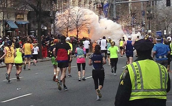 Runners continue to run towards the finish line of the   Boston Marathon as an explosion erupts near the finish line