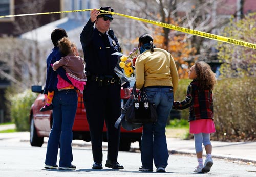 A Boston Police officer lifts the tape for a family to leave flowers in front of the home of the Richard family whose eight-year-old son, Martin, was killed by an explosion