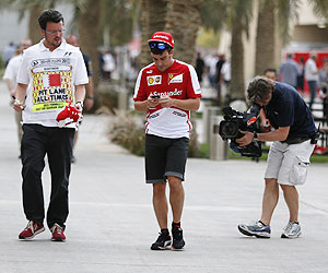 Ferrari'S Fernando Alonso (centre) checks his mobile phone in the paddock at the Bahrain International Circuit on Thursday