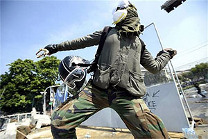 An anti-government protester throws a rock at Thai riot police as they attempt to remove barricades outside Government House in Bangkok on Monday