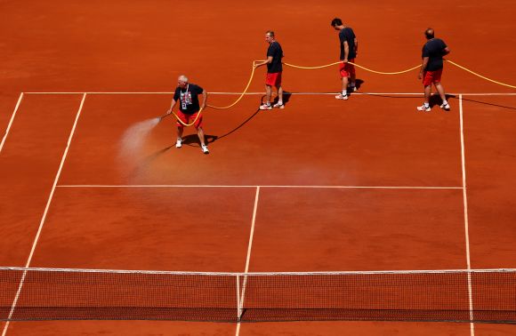 Court attendants water the clay on Court Philippe Chatrier during a break in the men's singles semi-final match between Novak Djokovic of Serbia and Rafael Nadal of Spain