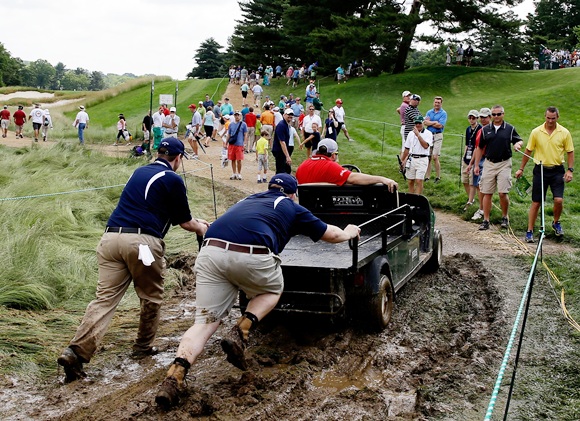 Staff help push a golf cart through the mud during the US Open at Merion Golf Club