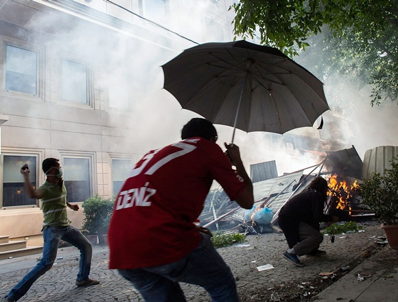 A protester throws an object from behind a burning barricade during a demonstration near Taksim Square
