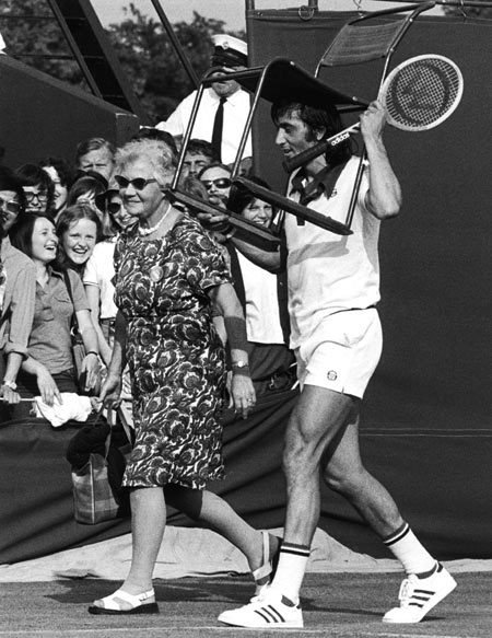 Ilie Nastase assists an elderly lady with her seat before a match, on July 2, 1975.