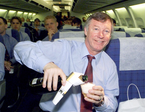 Manchester United manager Alex Ferguson celebrates his team's   victory over FC Juventus with a champagne toast on the return flight from Turin to Manchester