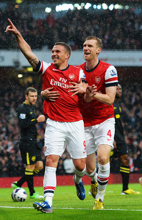 Lukas Podolski (left) of Arsenal celebrates with teammate Per Mertesacker (right) after scoring against Wigan Athletic on Tuesday