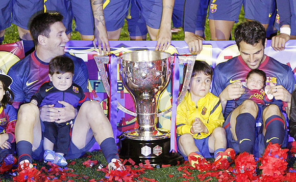 Lionel Messi and his son Thiago sits next to teammate Cesc Fabregas and his infant daughter Lia during the trophy presentation ceremony at the Camp Nou on Sunday