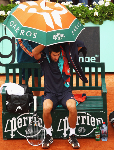 Novak Djokovic of Serbia shelters from the rain during the men's singles final against Rafael Nadal of Spain at Roland Garros on June 11, 2012