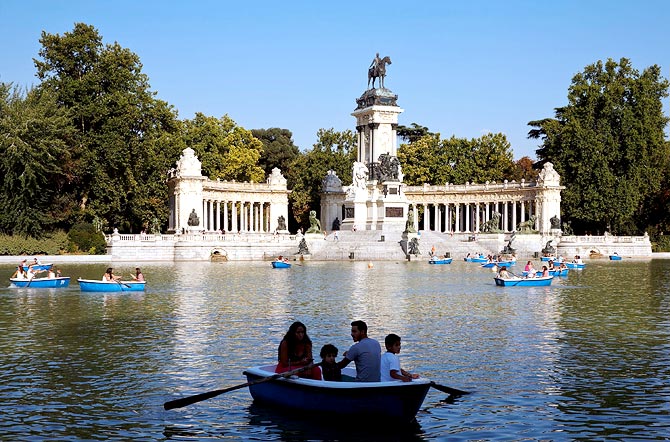 People on rowboats at the Retiro Park pond with Alfonso the Twelfth of Spain monument in the background in Madrid
