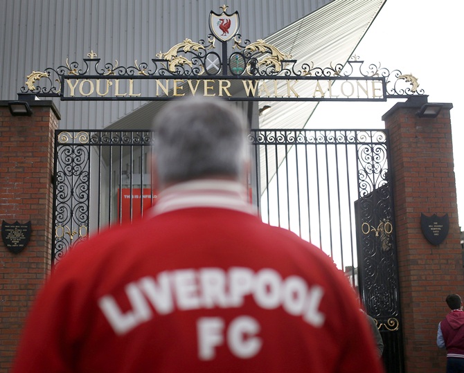 A Liverpool supporter stands in front of the Shankly gates outside Anfield in Liverpool