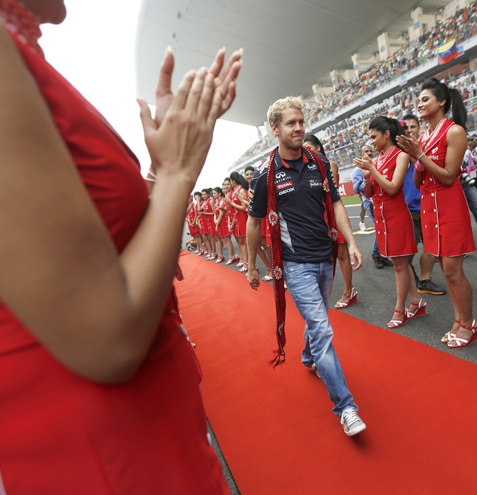 Grid girls clap as Red Bull Formula One driver Sebastian Vettel of Germany walks