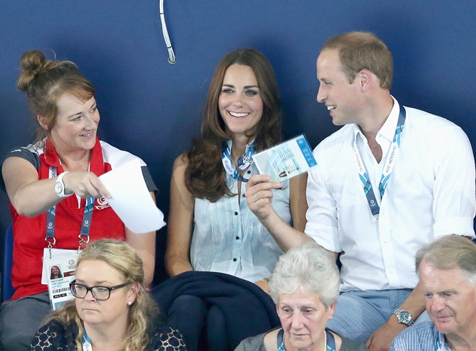 Catherine, Duchess of Cambridge, is fanned in the heat of Tollcross Swimming Centre by Prince William, Duke of Cambridge, and a Games volunteer as they watch the swimming