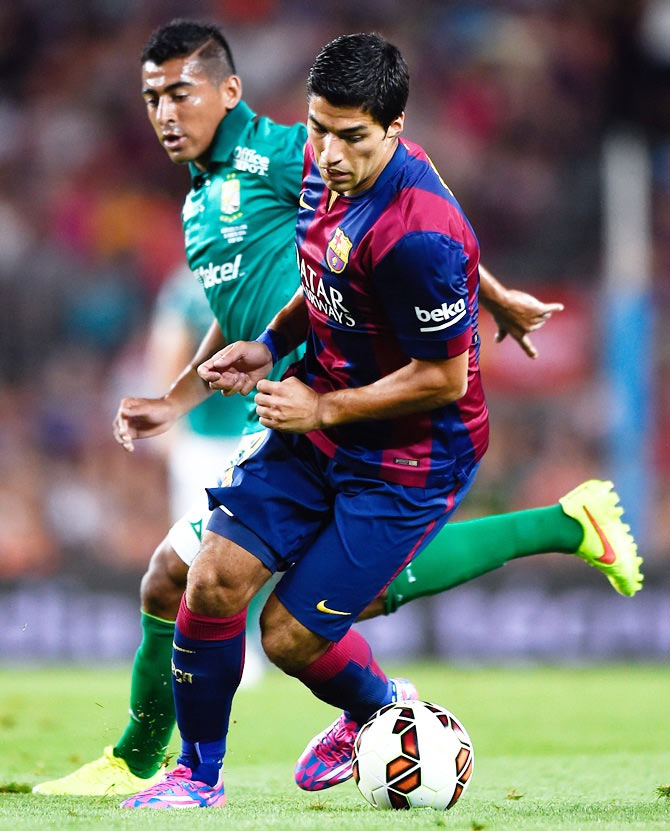 Luis Suarez of FC Barcelona competes for the ball with Luis Delgado of Club Leon