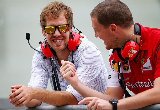Sebastian Vettel of Germany and Infiniti Red Bull Racing smiles as he speaks with members of the Ferrari team on the pit wall