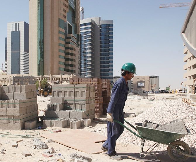 A worker uses a wheelbarrow to move cinder blocks on a construction site in Qatar
