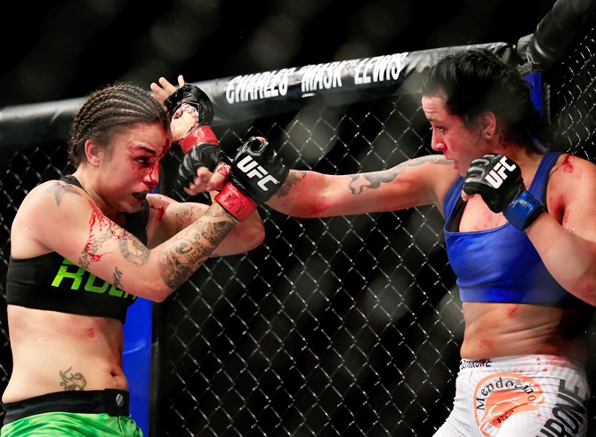 Raquel Pennington (green shorts) and Ashlee Evans-Smith (white shorts) grapple against the   cage in their fight during the UFC 181 event