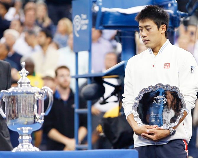 Kei Nishikori of Japan holds his runner up trophy as he looks at the winner's trophy after being defeated in the US Open men's singles final by Marin Cilic of Croatia