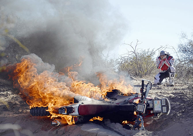 Paulo Goncalves of Portugal reacts in front of his Honda on fire during the fifth stage of the Dakar Rally 2014 from Chilecito to Tucuman, Argentina