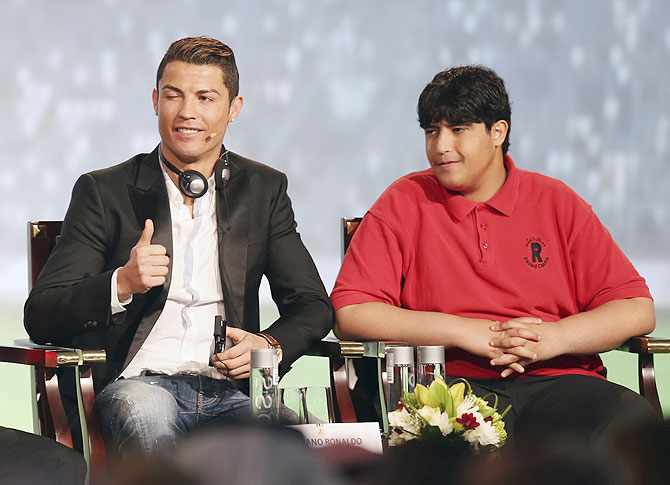 Cristiano Ronaldo (left), who plays for Real Madrid and Portugal's national soccer team, gestures as he sits next to a handicapped man, invited by conference organisers as a guest, during the eighth Dubai International Sports Conference, in Dubai on December 28, 2013