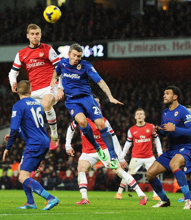 Per Mertesacker of Arsenal jumps with Kevin McNaughton of Cardiff City