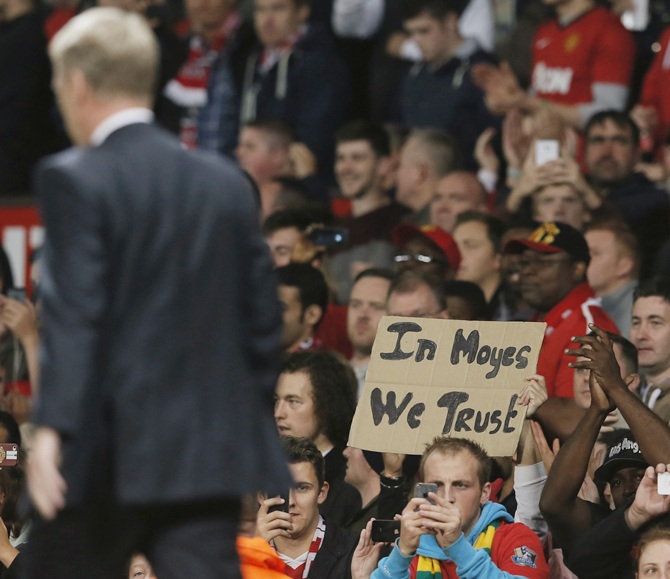 Manchester United's manager David Moyes walks to the dugout as a fan holds up a placard