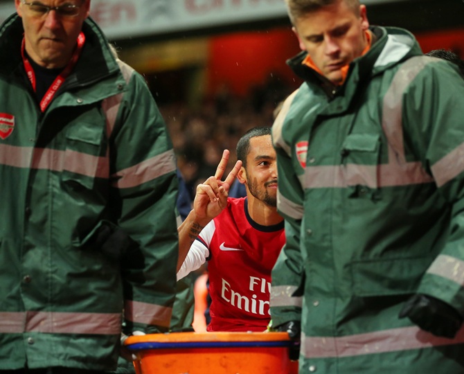 The injured Theo Walcott of Arsenal makes a 2-0 gesture to the Tottenham fans as he is stretchered off the pitch