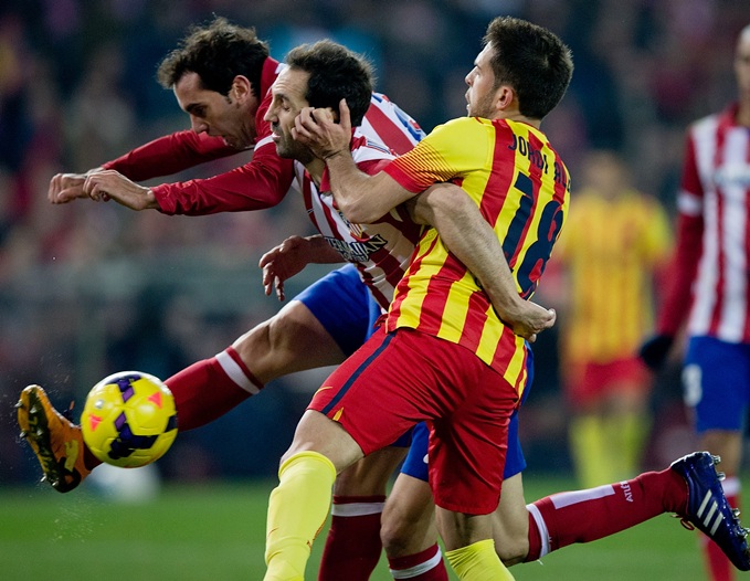 Jordi Alba (right) of FC Barcelona holds the ear of Juan Francisco Torres (second left) of Atletico de Madrid as his teammate Diego Godin (left) strikes the ball