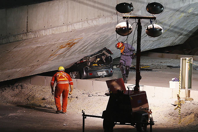 Rescue workers inspect a car trapped underneath a bridge that collapsed while under construction in Belo Horizonte on Thursday