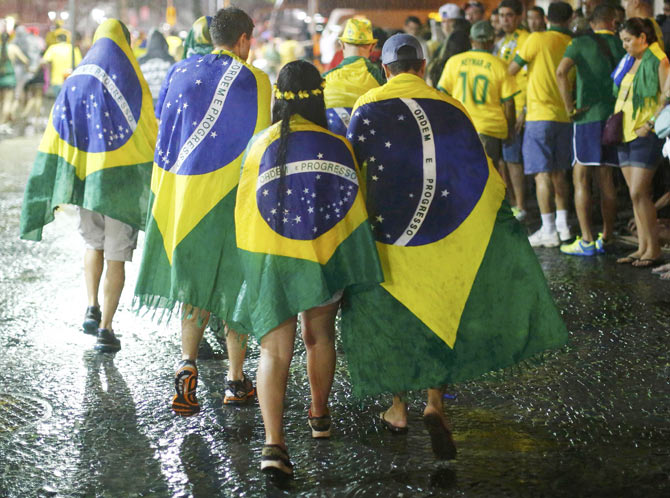 Brazil soccer fans walk in the rain after watching a broadcast of their team's loss against Germany in their 2014 World Cup semi-final match, in Rio de Janeiro on Tuesday