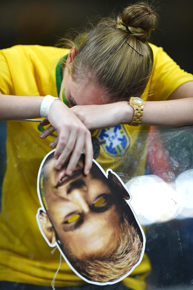 A dejected Brazil fan holding a Neymar mask reacts
