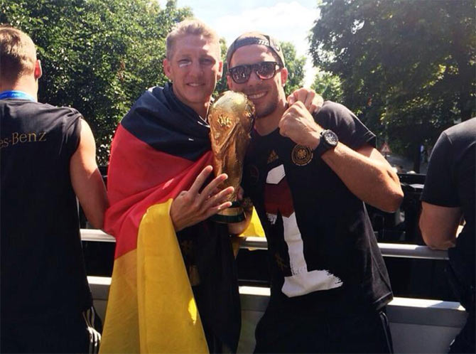 Lukas Podolski and Bastian Schweinsteiger celebrate with the World Cup atop the bus on Tuesday