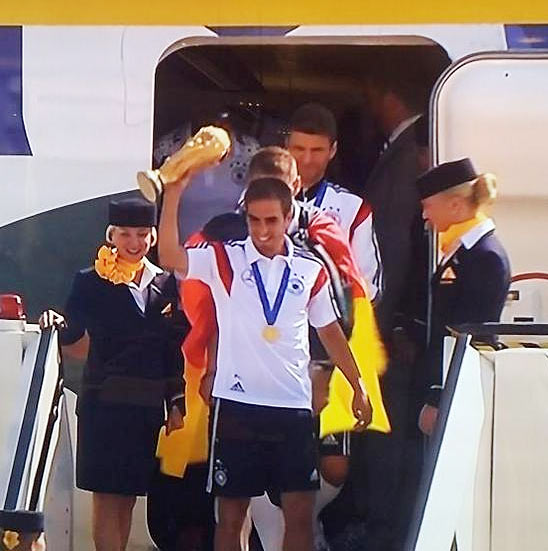 Germany captain Philipp Lahm shows off the trophy as he leads his team out of the aircraft on arrival in Berlin on Tuesday