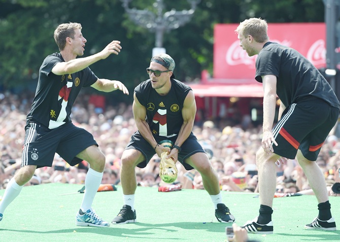 Per Mertesacker, right, Lukas Podolski, centre, and Thomas Meuller, left, celebrate on stage