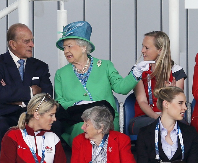 Britain's Queen Elizabeth gestures to her husband Prince Philip, left, as they take their   seats ahead of women's preliminary hockey match between England and Wales