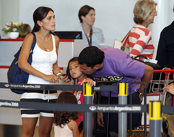 Argentine soccer player Carlos Tevez waits in the check-in line with his wife Vanesa Mansillo (left), and daughters Katie and Florencia (in red)