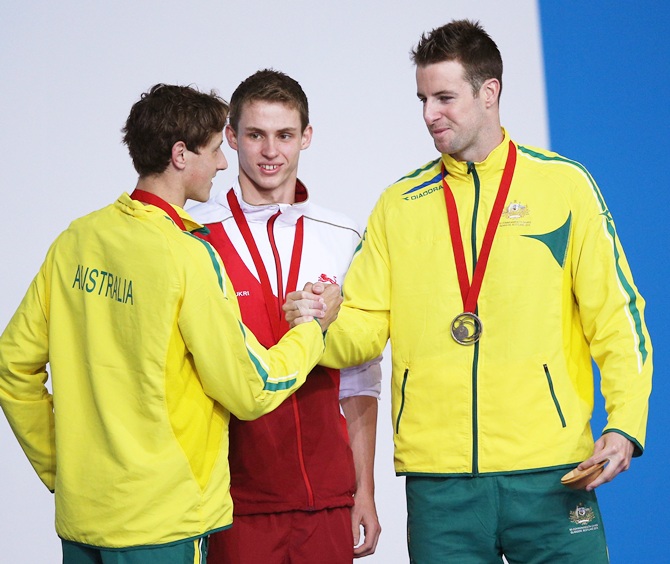 Gold medallist Benjamin Proud of England watches as silver medallist Cameron McEvo, left of Australia shakes hands with bronze medallist James Magnussen of Australia