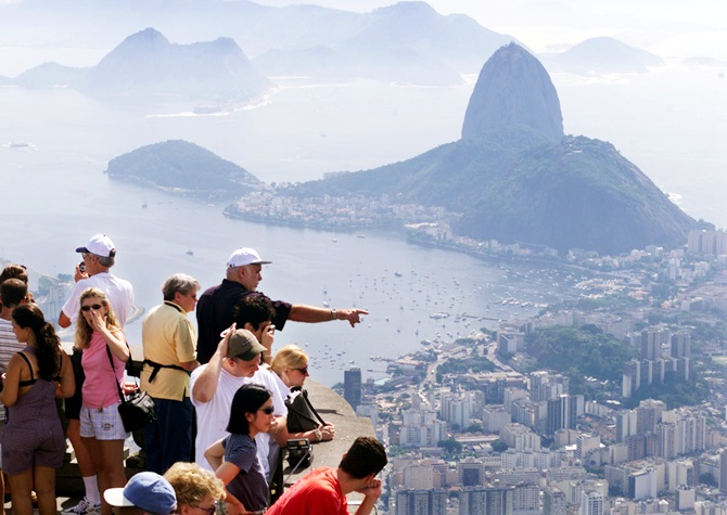 Tourists take in the scene from atop scenic Corcovado mountain in Rio de Janeiro. Sugarloaf mountain and Botafogo beach can be seen in the background