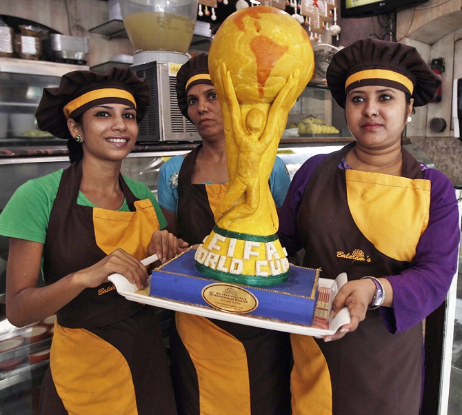 Workers pose with a replica of the one and half feet tall and six kg FIFA World Cup trophy, made from sweets