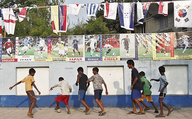Children play soccer in front of a wall, decorated with pictures of international footballers and their national flags, on the outskirts of Kolkata