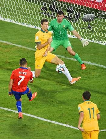Alexis Sanchez of Chile shoots and scores his team’s first goal past Australia’s Matthew Spiranovic and goalkeeper Mathew Ryan.