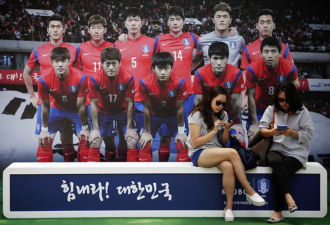 Women use their mobile phones in front of a board with a picture of the South Korean national soccer team in Seoul on Tuesday