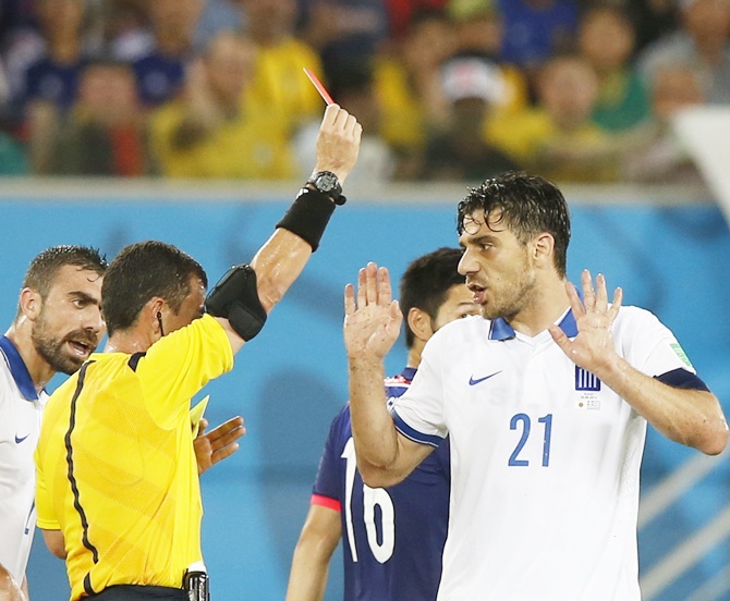 Greece's Kostas Katsouranis, right, is shown a red card by referee Joel Aguilar of El Salvador