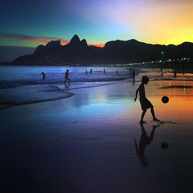A young boy plays football at sunset on the beach in Rio de Janeiro.