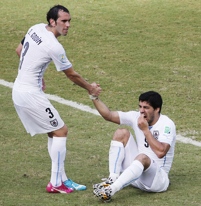 Uruguay's Luis Suarez (R) holds his teeth while sitting on the ground as teammate Diego Godin helps him up during their match against Italy at the Dunas arena in Natal on Tuesday