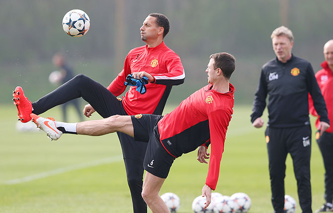 Rio Ferdinand and Jonny Evans of Manchester United compete for the ball as team manager David Moyes watches during a training session at the Aon Training Complex in Manchester on Monday