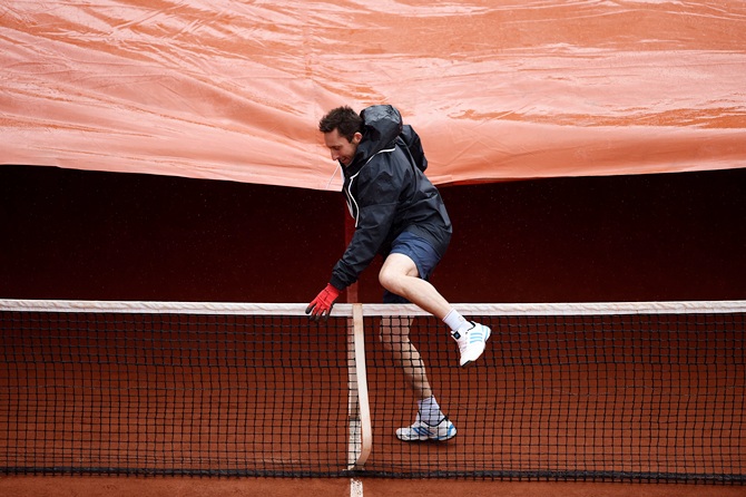 A groundsman pulls the rain cover over the net on Court Suzanne Lenglen as rain interrupts play