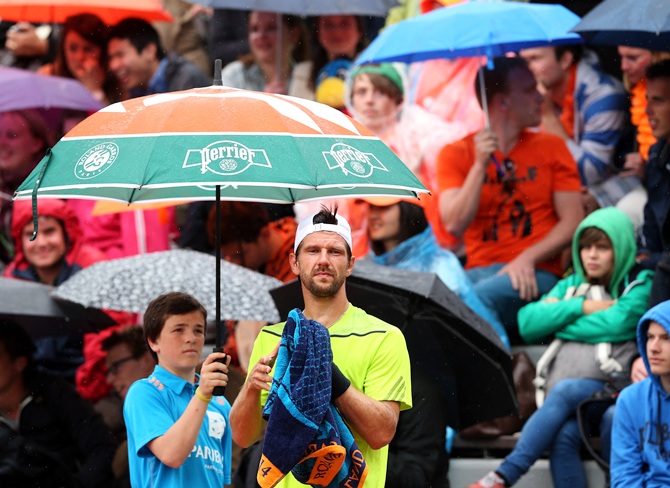 Jurgen Melzer of Austria waits for play to start as he shelters from the rain   under an unbrealla during his men's singles match against David Goffin of Belgium on day two of the French Open